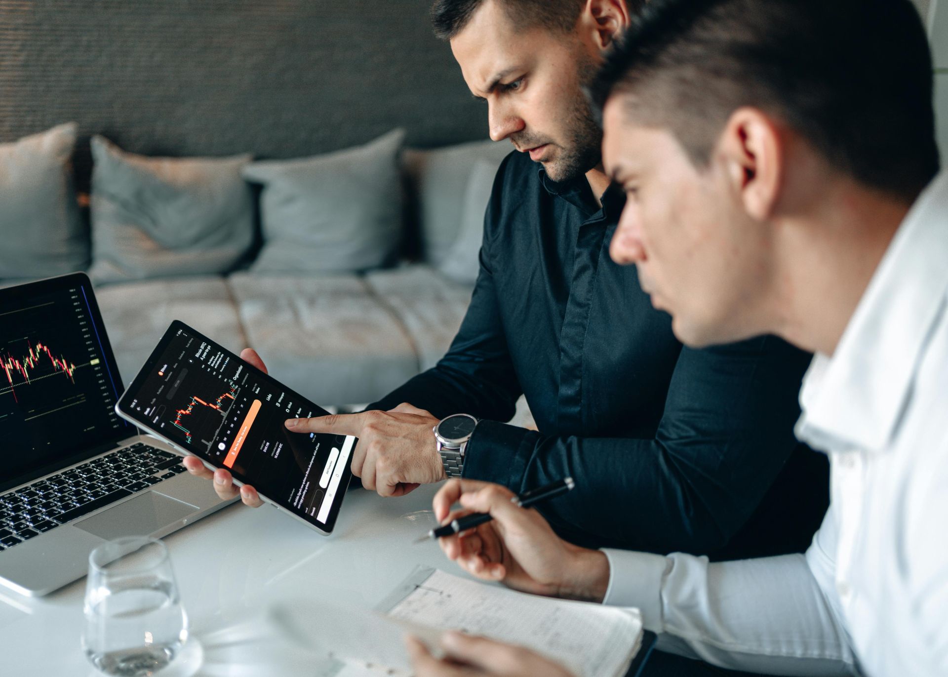 Two business professionals using a laptop and tablet to analyze online trading data indoors.